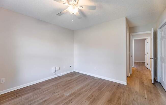 A room with a ceiling fan and light fixture, hardwood floors, and white walls.