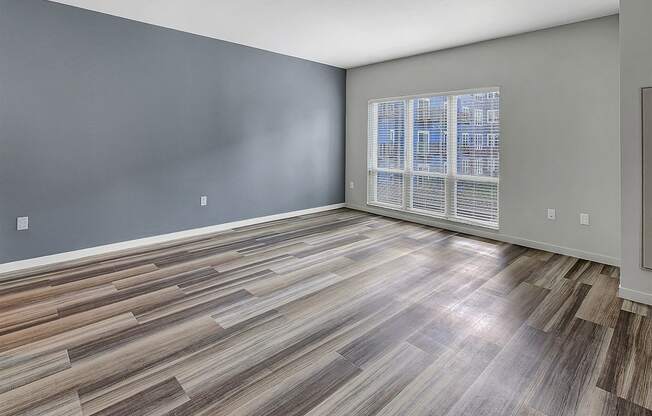 an empty living room with a large window and wooden floors