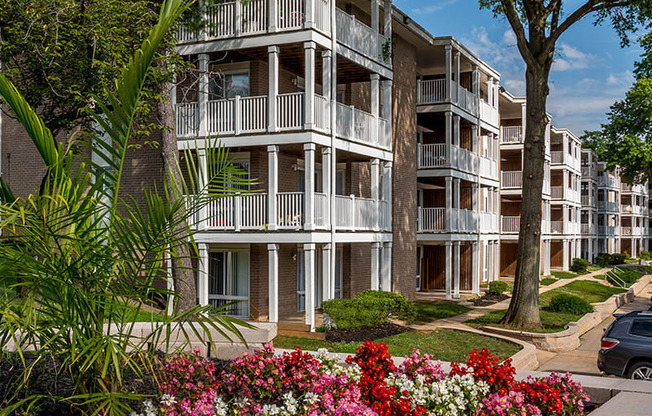 a picture of an apartment complex with trees and flowers in the foreground