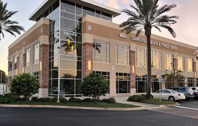 An exterior view of the Gainesville Health & Fitness Center with palm trees and a parking lot near The Flats at Tioga Town Center apartments.