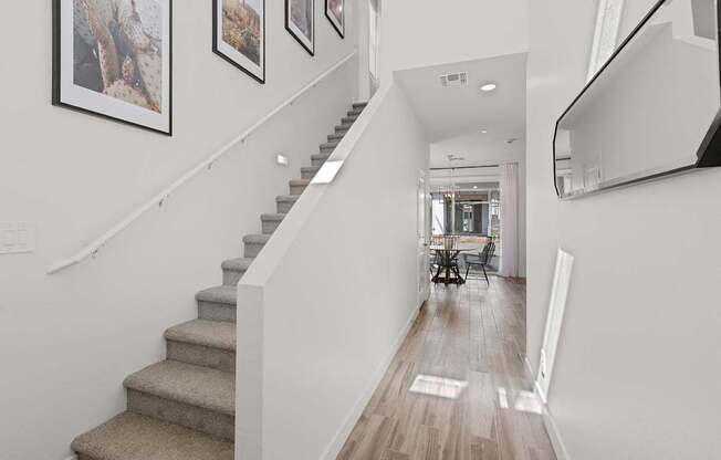 A staircase with a beige carpeted runner and white walls with framed pictures.