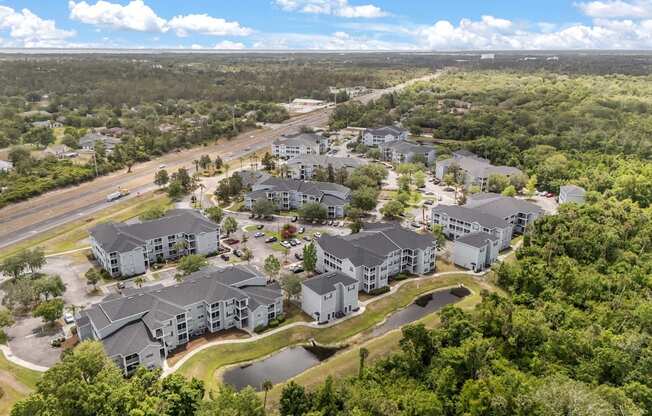 A bird's eye view of a residential complex surrounded by greenery and a highway.