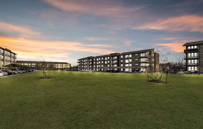 A large grassy field in front of a building with a sunset in the background.