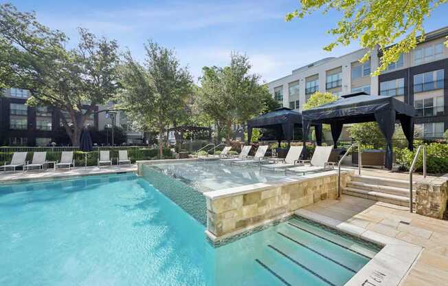 A swimming pool with a hot tub and lounge chairs.