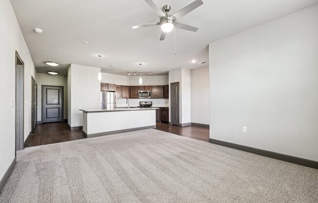 A spacious living room with a carpeted floor and a ceiling fan.