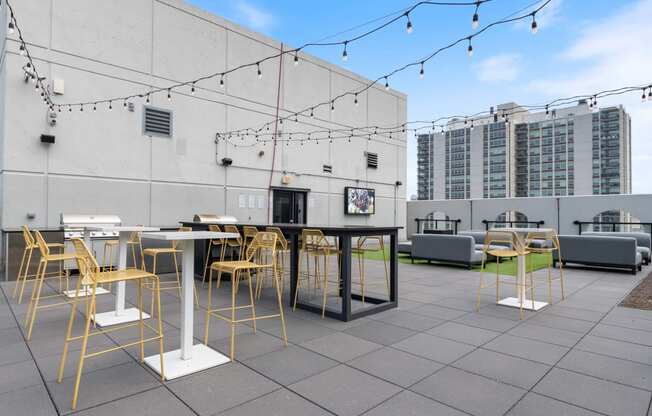 a rooftop patio with tables and chairs and buildings in the background