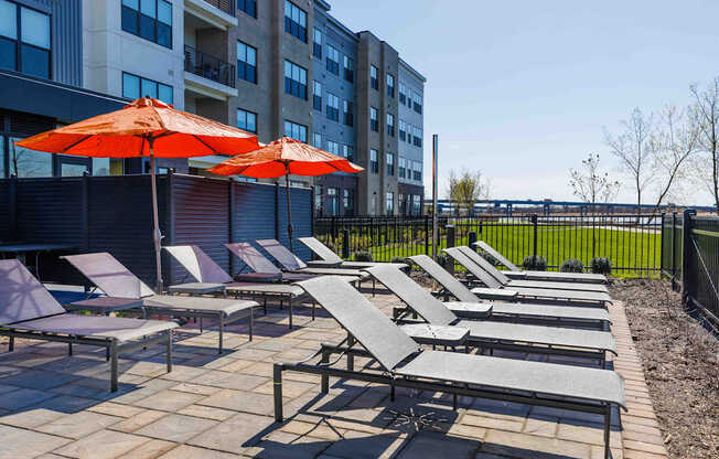 A row of sun loungers and umbrellas are set up on a patio.
