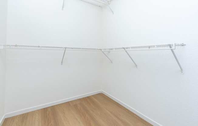 an empty room with white walls and wooden flooring and a white closet with shelves