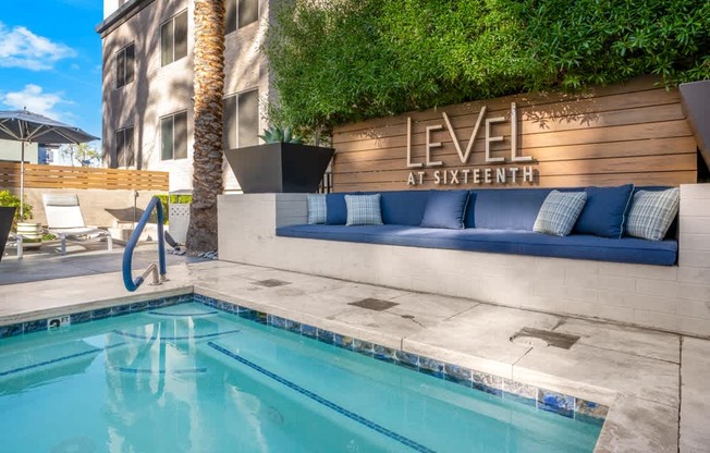 A pool with a blue tiled edge and a poolside seating area with a couch and a palm tree.