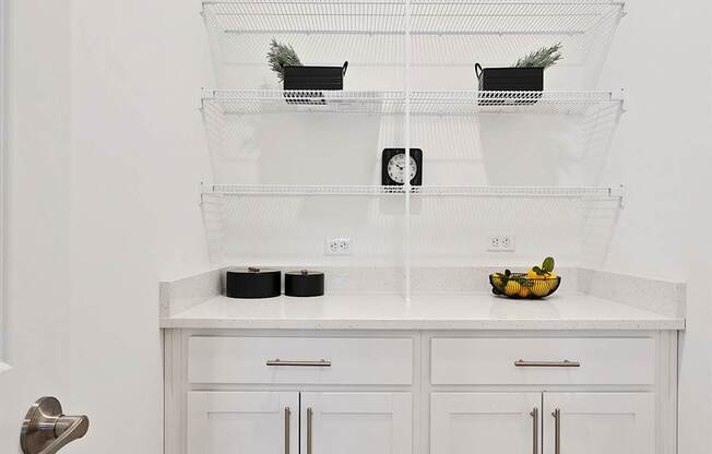 A kitchen with white cabinets and a white countertop with a bowl of fruit on it.