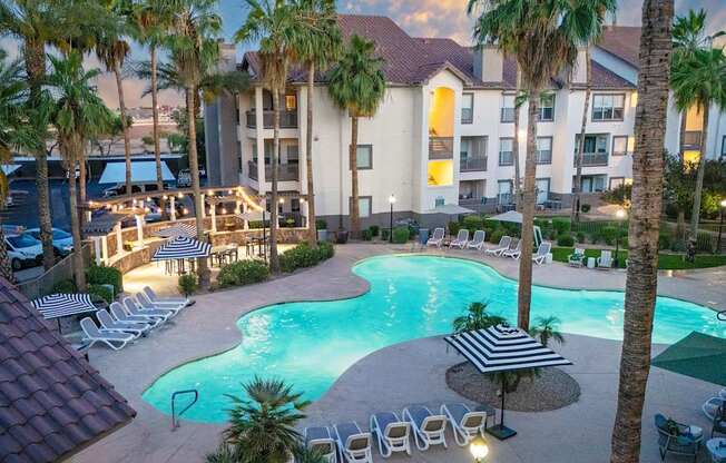 A pool surrounded by palm trees and lounge chairs.