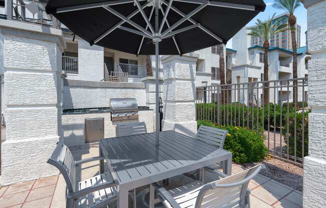 Outdoor bbq grill area with a table and chairs and umbrella