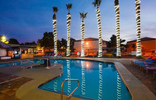 a swimming pool at night with palm trees in the background