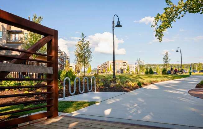 A large green space with a walking trail, path lights, trees, bike station, and bridge near River Station apartment buildings.