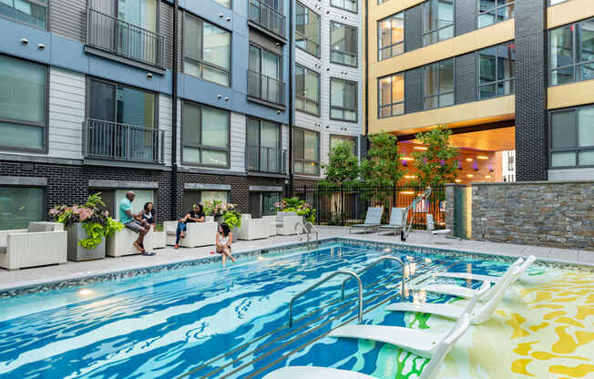 A swimming pool in a residential building with people relaxing by the poolside.