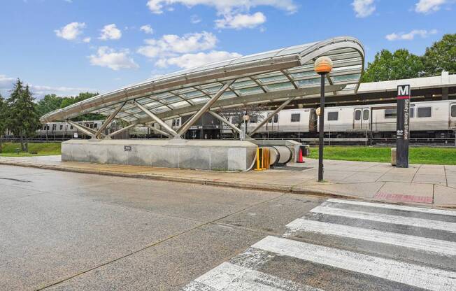 A train station with a train on the tracks and a pedestrian crossing in front.