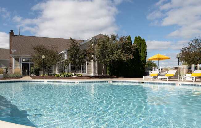A swimming pool in front of a house with a yellow umbrella.