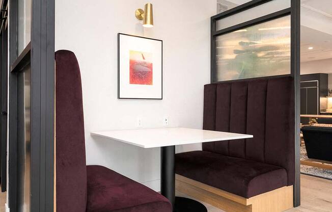 A white table with a red chair and a framed picture of a drink on the wall.