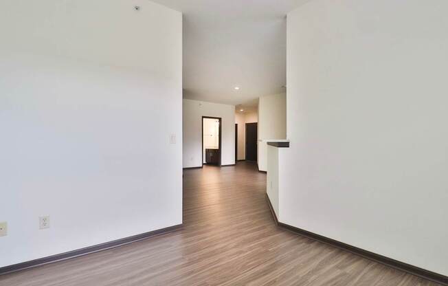 A long, empty hallway with white walls and wood flooring.