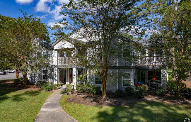 A white house with a porch and a tree in front.