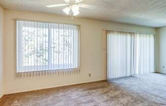 Apartments Near Ocean Beach - Terrace View -Empty Living Room with Large Window, Sliding Glass Door, Ceiling Fan, and Carpet at Terrace View Apartments, California