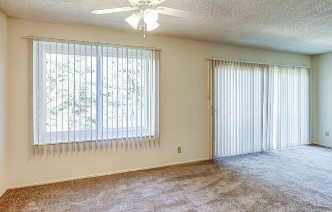 Apartments Near Ocean Beach - Terrace View -Empty Living Room with Large Window, Sliding Glass Door, Ceiling Fan, and Carpet at Terrace View Apartments, California