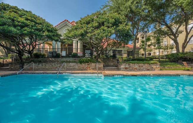 A swimming pool in front of a house with trees.