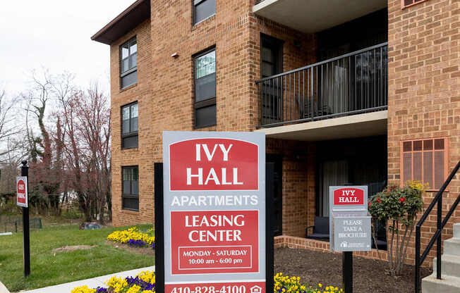 A sign for Ivy Hall Apartments leasing center in front of a brick building.