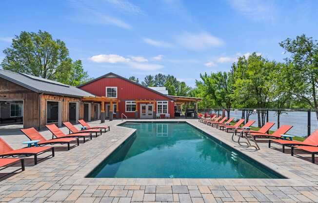 A pool surrounded by red lounge chairs and a wooden building.