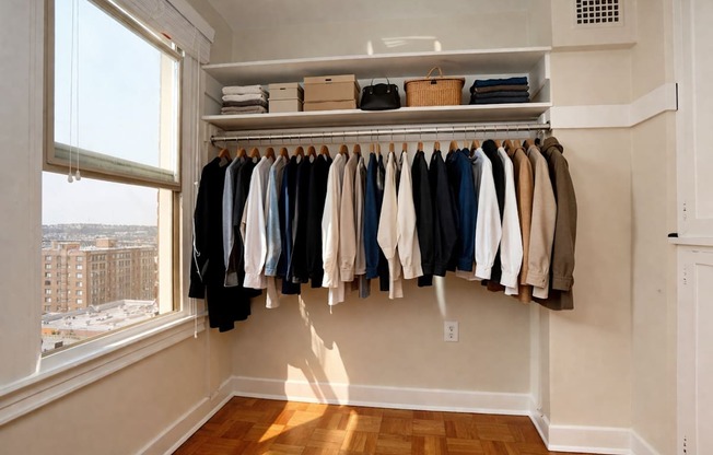 A white closet with clothes hanging up and a window letting in sunlight.