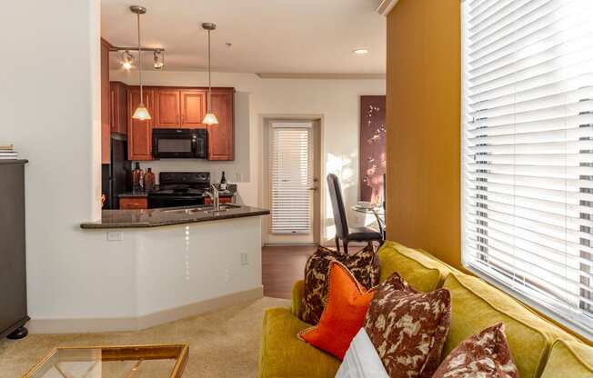 a living room with a yellow couch and a kitchen in the background