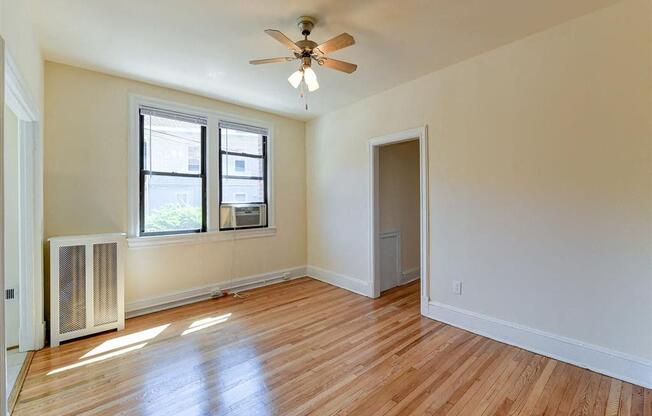 vacant living area with hardwood flooring, large windows and ceiling fan at the klingle apartments in washignton dc