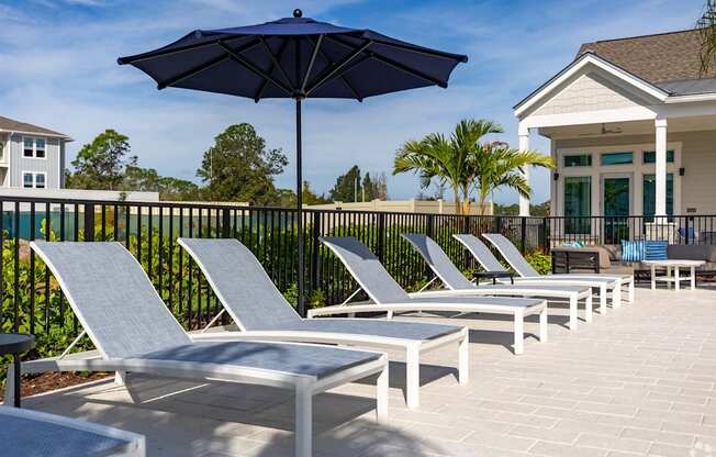 a row of lounge chairs and umbrellas on a patio with a house