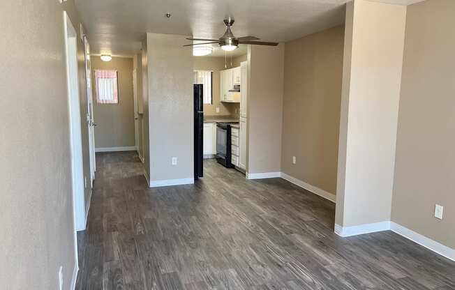 an empty living room with a ceiling fan and a kitchen in the background