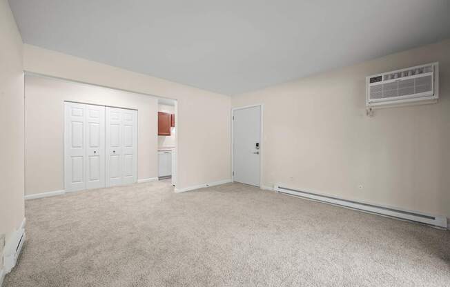 A room with a carpeted floor, two doors, and an air conditioning unit on the wall.