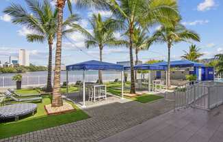 A sundeck area with palm trees and a blue canopies with seating at Blue Lagoon 7 Apartments in Miami, FL