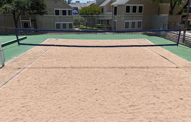 A sand volleyball court with a green fence around it.