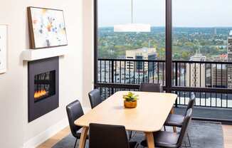 A table with chairs and a fireplace in a room with a view of the city.