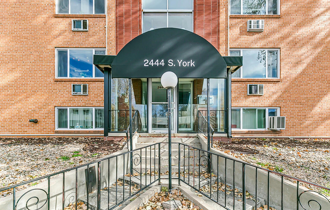 Charming apartment entrance with classic brick facade and modern awning, featuring well-maintained landscaping and inviting walkways.