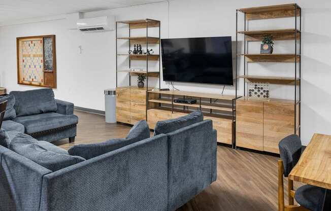 A living room with a grey couch, a television, and a wooden shelf.