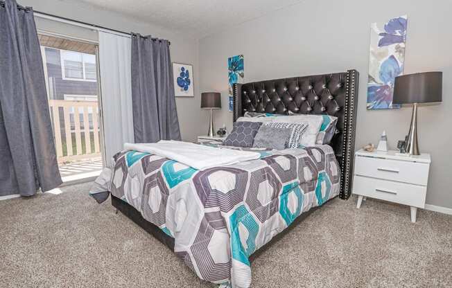 Model bedroom with large bed and window letting in natural light at Maplewood apartments in Shreveport, LA.