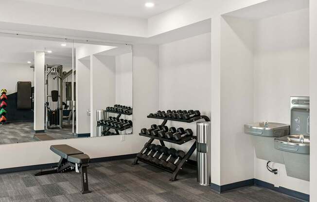 A gym room with a bench, weights, and a mirror.