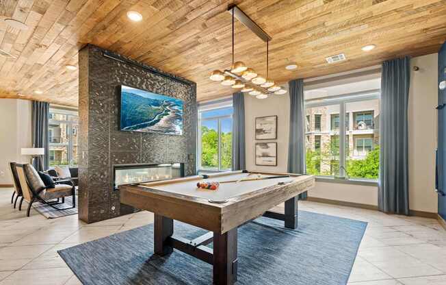 A billiard table is in the middle of a room with a fireplace and a TV above it.