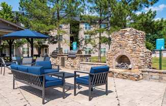 A patio with a stone fireplace and two chairs.