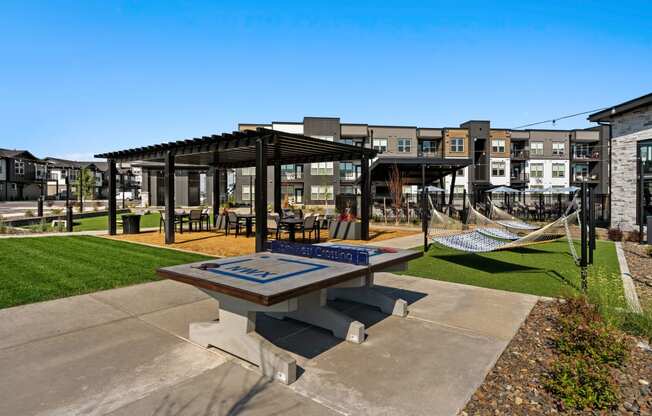 a picnic area with a table and hammocks in front of an apartment building