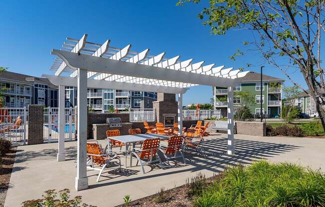 A white pergola with orange chairs is in front of a building.