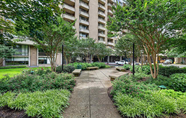 A concrete walkway leads through a landscaped area with a large building in the background.