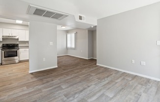 the living room and kitchen of an apartment with white walls and wood flooring