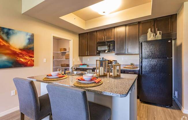 A kitchen with a black refrigerator and a painting of a sunset on the wall.