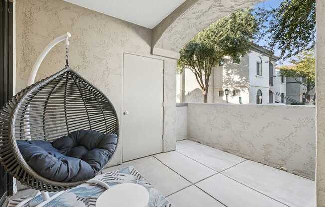 A hanging egg chair with a cushion is in the foreground of a patio area.